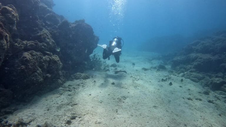 Scuba diver swimming through a rocky underwater passage with sunlight filtering from above, featured in the blog post ‘PADI Certifications, Why Get your Scuba diving PADI license in Costa Rica?’