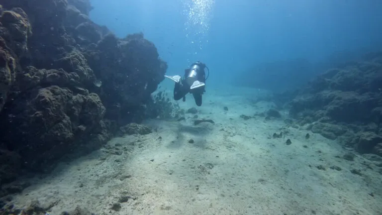 Scuba diver swimming through a rocky underwater passage with sunlight filtering from above, featured in the blog post ‘PADI Certifications, Why Get your Scuba diving PADI license in Costa Rica?’