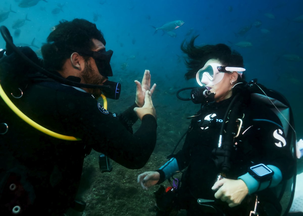 Dive instructor underwater demonstrating a two-hand scuba signal to a student diver.
